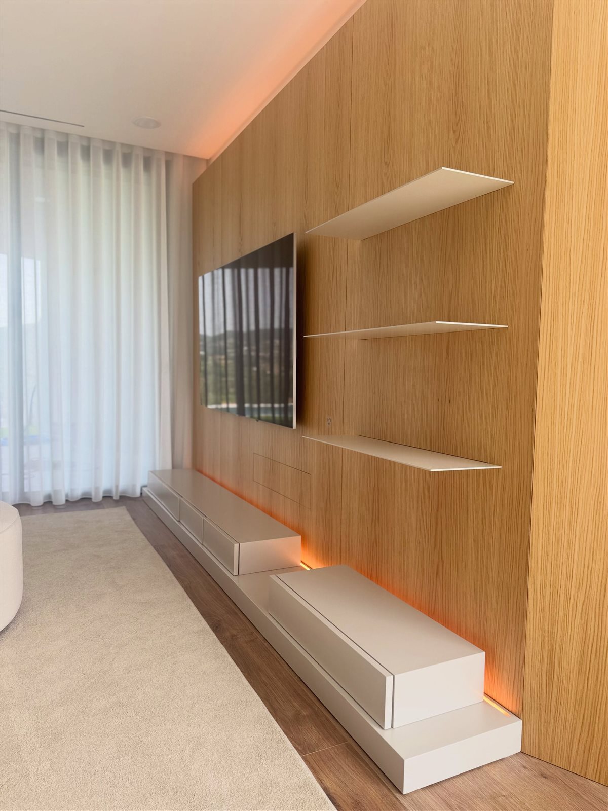 Sala com painel de madeira, lacado claro e iluminação inferior